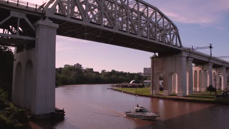 The-Cuyahoga-River-around-dusk-where-a-boat-passes-under-a-train-trestle-bridge