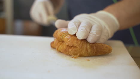 Man-hand-cutting-freshly-baked-croissant-with-long-knife-in-bakery