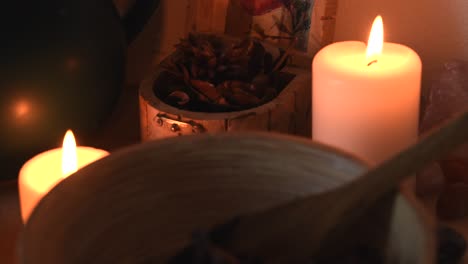 Relaxing-background-detail-shot-of-an-herbal-tea-shop,-with-candles-with-flickering-flames,-herbs,-a-wooden-bowl-and-some-dust-flying-around