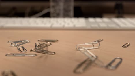 A-hand-full-of-paper-clips-slowly-dropping-onto-an-office-desk-a-little-bit-at-a-time