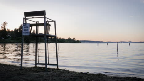 Handheld-shot-of-empty-lifeguard-stand-overlooking-calm-lake-at-sunset-with-sign-saying-"NO-WATERCRAFT-ALLOWED