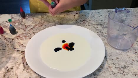 Small-hands-dropping-different-colors-of-food-coloring-onto-a-plate-of-white-milk