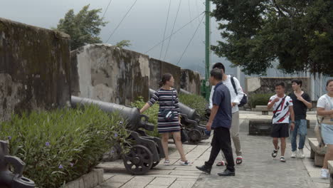 Tourists-passing-by-near-old-metal-artillery-cannons-on-top-of-Fortaleza-do-Monte-in-Macau,-Macau-SAR,-China
