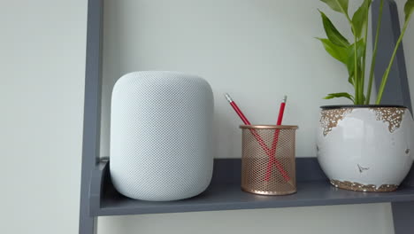Panning-Left-Shot-of-an-Apple-HomePod-on-top-of-Modern-Looking-Bookshelf-adjacent-to-a-Pencil-Holder---Plant