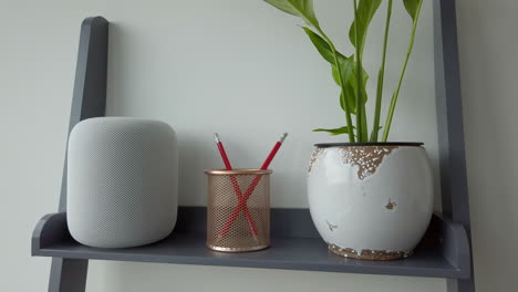 Slow-Motion-Static-Shot-of-Man-Double-Tapping-an-Apple-HomePod-on-top-of-Modern-Looking-Bookshelf-adjacent-to-a-Pencil-Holder---Plant