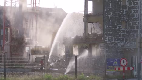 Excavator-is-demolishing-the-old-building-and-the-worker-with-a-hosepipe-is-spraying-water-in-order-to-prevent-smoke