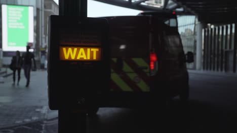 Close-up-shot-of-a-Pedestrian-crossing-machine-illuminated-wait-sign-with-a-red-London-bus-passing-by