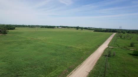 Aerial-pass-over,-rural-landscape-grasslands,-trees,-dirt-road-and-water-tank-Kansas,-Missouri