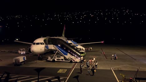Aeroplane-landing-Passengers-leaving-arrival-airplane,-disembarkation-Night-time-Airport-operation,-PBB-staircase-moves-towards-aeroplane-to-support-secure-safety-offloading-exit-dark-sky-lights