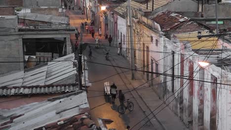 Birds-eye-view-down-on-typical-Cuban-street-life-at-dusk-with-soft-street-lights,-electricity-and-telephone-cables-hanging,-children-playing,-adults-walking-and-motorcycles-passing-by
