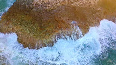 Tilting-up-aerial-shot-of-foamy-waves-hitting-a-cliff-at-sunset