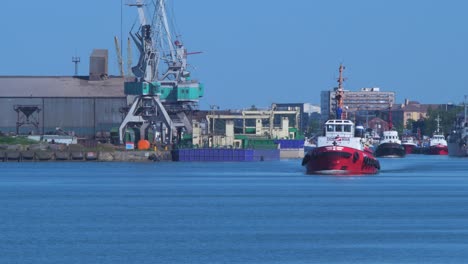 Harbour-tug-leaving-Port-of-Liepaja-in-hot-sunny-day,-port-cranes-in-background,-wide-shot-from-a-distance