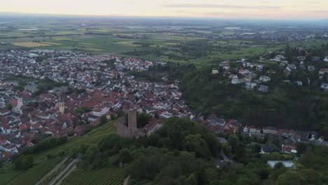 Flying-over-Strahlenburg-castle-in-the-German-city-of-Schriesheim-with-aerial-view-of-valley-and-town-during-sunset