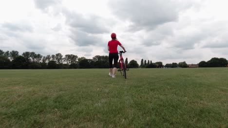 Caucasian-female-cyclist-in-red-top-walking-with-her-bike-in-a-park-in-slow-motion