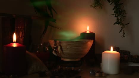 Detail-of-a-potion-making-witch-room,-with-green-steam-coming-out-from-a-wooden-bowl,-animal-teeth-hanging-from-it,-candles-with-flickering-flames,-old-books,-glasses-and-herbs-in-the-background