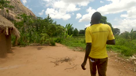 Kamerafahrt-Von-Hinten-Eines-Afrikanischen-Mannes,-Der-Durch-Ein-Ländliches-Dorf-In-Uganda-Geht