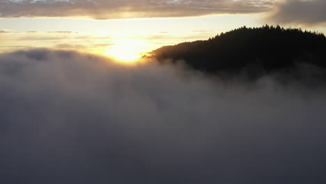 Drohnenflug-Durch-Nebel,-Der-Immergrüne-Bedeckte-Berge-Und-Einen-Goldenen-Sonnenuntergang-Enthüllt