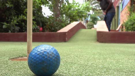 Close-and-Low-Shot-of-a-Golf-Ball-Being-Chipped-Over-an-Obstacle-and-Hitting-the-Pin-on-the-Green-at-the-Mini-Golf-Course