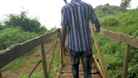 A-slow-motion-tracking-shot-of-a-young-African-man-crossing-over-a-wooden-foot-bridge-in-tropical-East-Africa