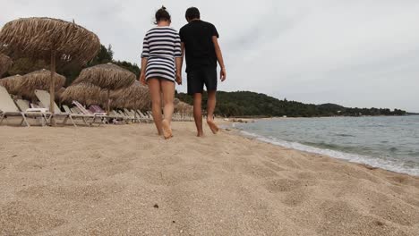 Couple-walking-on-a-beach-shore,-holding-hands