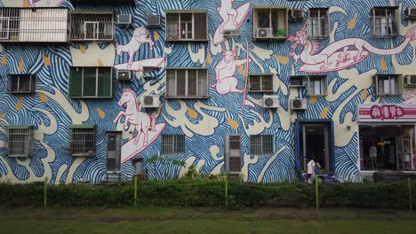 An-LRT-train-passing-a-street-art-wall-mural-at-Pier-2-Art-District-in-Kaohsiung,-Taiwan