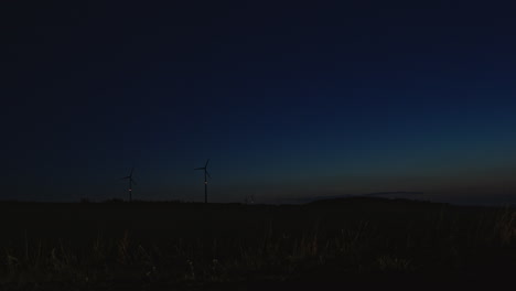 Wind-turbines-at-the-horizon,-almost-dark-blue-night-sky-with-car-passing-by