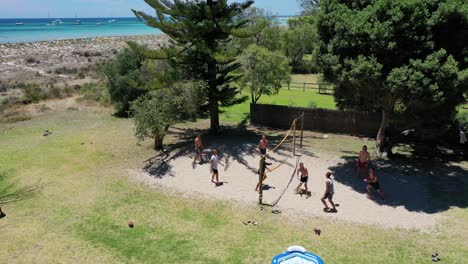 Aerial-View-of-People-Playing-Volleyball-on-Sand-Under-Tree-Shades-by-the-Sea-on-Sunny-Day