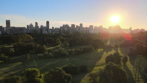Aerial-dolly-in-of-green-Municipal-golf-course-in-Palermo-neighborhood-with-buildings-in-background-at-sunset,-Buenos-Aires