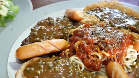 Close-Up-Footage-of-Combo-Steak-Included-Beef,-Fried-Fish-and-Sausages-Topped-With-Fresh-Pepper-Gravy-and-Spaghetti-Red-Sauce