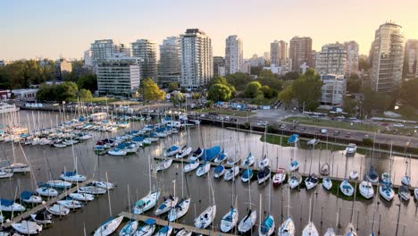 Aerial-dolly-in-of-sailboats-parked-inline-in-Olivos-Port-and-buildings-in-background-at-sunset,-Buenos-Aires