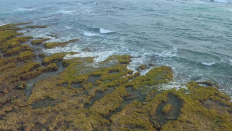 Drone-view-of-waves-on-Bai-Bang-beach,-with-moss-covered-on-rocks,-Phu-Yen-province,-central-Vietnam