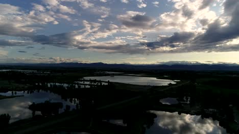 Atemberaubende-Herrlichkeit-In-Diesem-Sonnenuntergang-Mit-Wolken,-Die-Sich-In-Seen-Mit-Den-Felsigen-Bergen-Im-Hintergrund-Spiegeln
