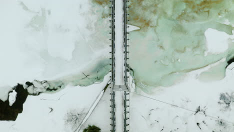 Top-down-View-Of-Simple-Suspension-Bridge-Across-Icy-River-At-Winter-Season-In-Haugastol,-Norway