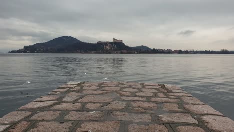 Seagulls-fly-away-from-pier-overlooking-Maggiore-lake-and-Angera-fortress