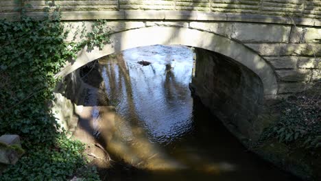Un-Río-Que-Fluye-Suavemente-Bajo-Un-Viejo-Puente-De-Piedra