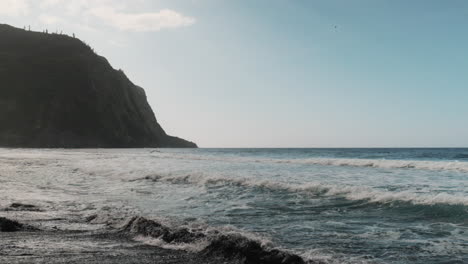 Slow-motion-shot-of-Waipi'o-Valley-with-blue-ocean-waves-and-black-sandy-beach-during-blue-sky