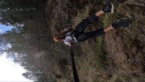 Vertical-action-camera-shot-of-a-young-man-gliding-down-in-high-speed-on-a-zipline-in-Canada-with-beautiful-lush-green-forest-around-him