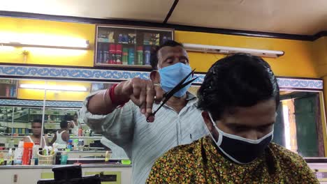 Indian-barber-cutting-hair-of-young-male-wearing-masks-during-lockdown,-quarantine-during-corona-virus-or-covid-19