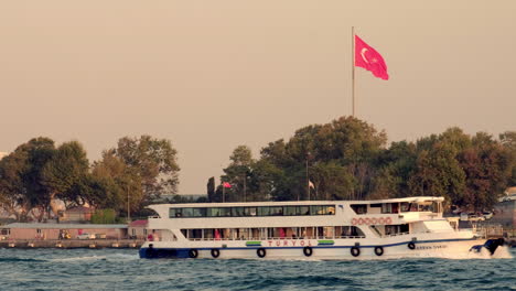 Kleine-Istanbuler-Fähre-Passiert-Riesige-Türkische-Flagge-Bei-Sonnenuntergang