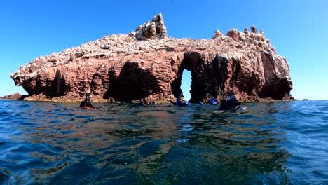 Snorkelers-float-in-the-water-just-offshore-from-an-arch-rock-formation-near-La-Paz,-Mexico