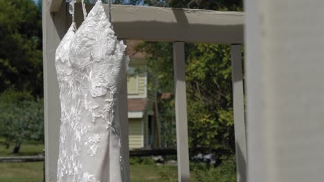 Beautiful-designer-wedding-dress-hanging-from-a-pergola-outside-on-a-sunny-day