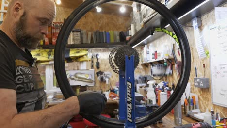 Male-bike-mechanic-trues-a-wheel-in-a-workshop