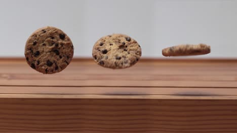 Three-Chocolate-Chip-Cookie-Spinning-and-Rolling-in-the-Air-above-Wooden-Table,-4K