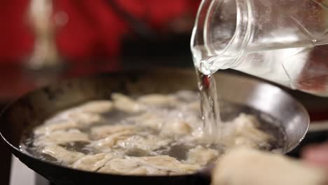 Close-up-shot-of-a-chef-pouring-water-into-a-wok-cooking-dumplings