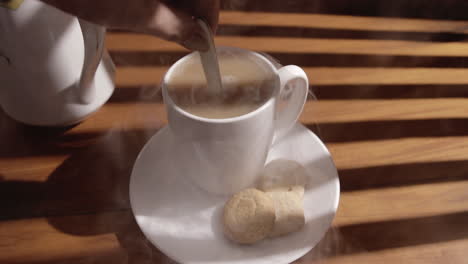 Hand-Stirring-Steaming-Coffee-In-A-Cup-On-Saucer-With-Cookies