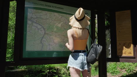 Back-of-Young-Woman-Looking-at-Map-of-Bohemian-Switzerland-National-Park,-Czech-Republic-on-Sunny-Day