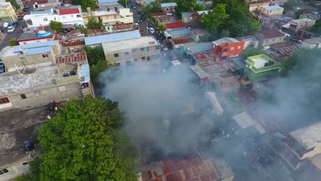 Aerial-view-around-a-smoking-building,-burning-on-a-crowded-city-street---circling,-drone-shot