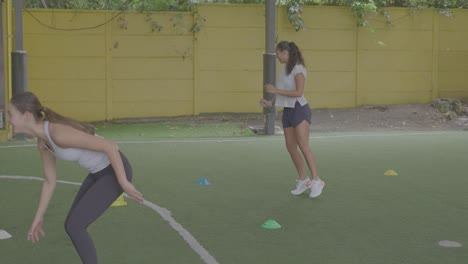 Mädchen-Trainieren-Auf-Fußballplatz-Mit-Kegeln,-Die-Kniebeugen-Auf-Grünem-Kunstrasen-Machen