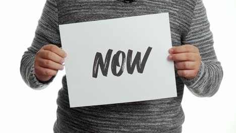 A-person-holding-a-sign-with-a-message-and-the-word-"now