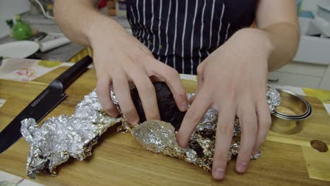Chef-unwraps-baked-beetroot-from-foil-paper-on-kitchen-table,-close-up-slow-motion